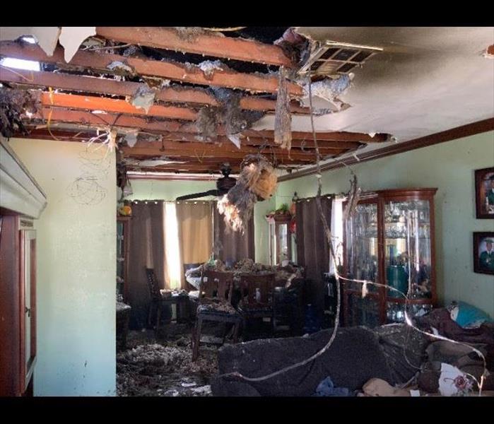 A living room with hole in the ceiling showing smoke damage and black soot on furniture and walls