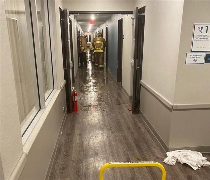 A wet hallway with firefighters walking it. 